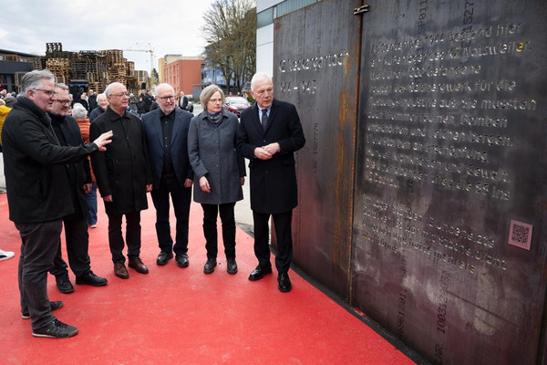 rechts eine Wand aus Cortenstahl mit Inschriften über die Geschichte des KZ Neckargartach, links stehen im Halbkreis 6 Personen