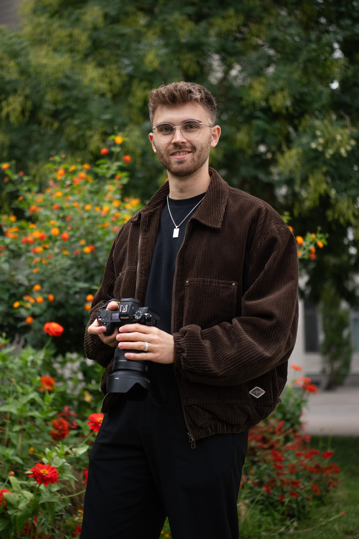 ein junger Mann mit Brille hält eine Fotokamera
