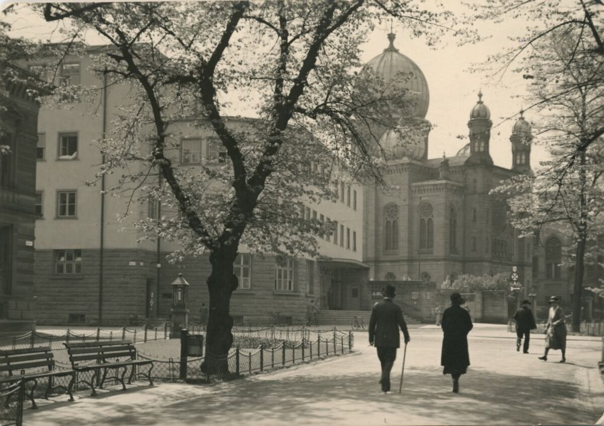 links steht die Hauptpost, weiter rechts die Synagoge, zwei Menschen spazieren davor